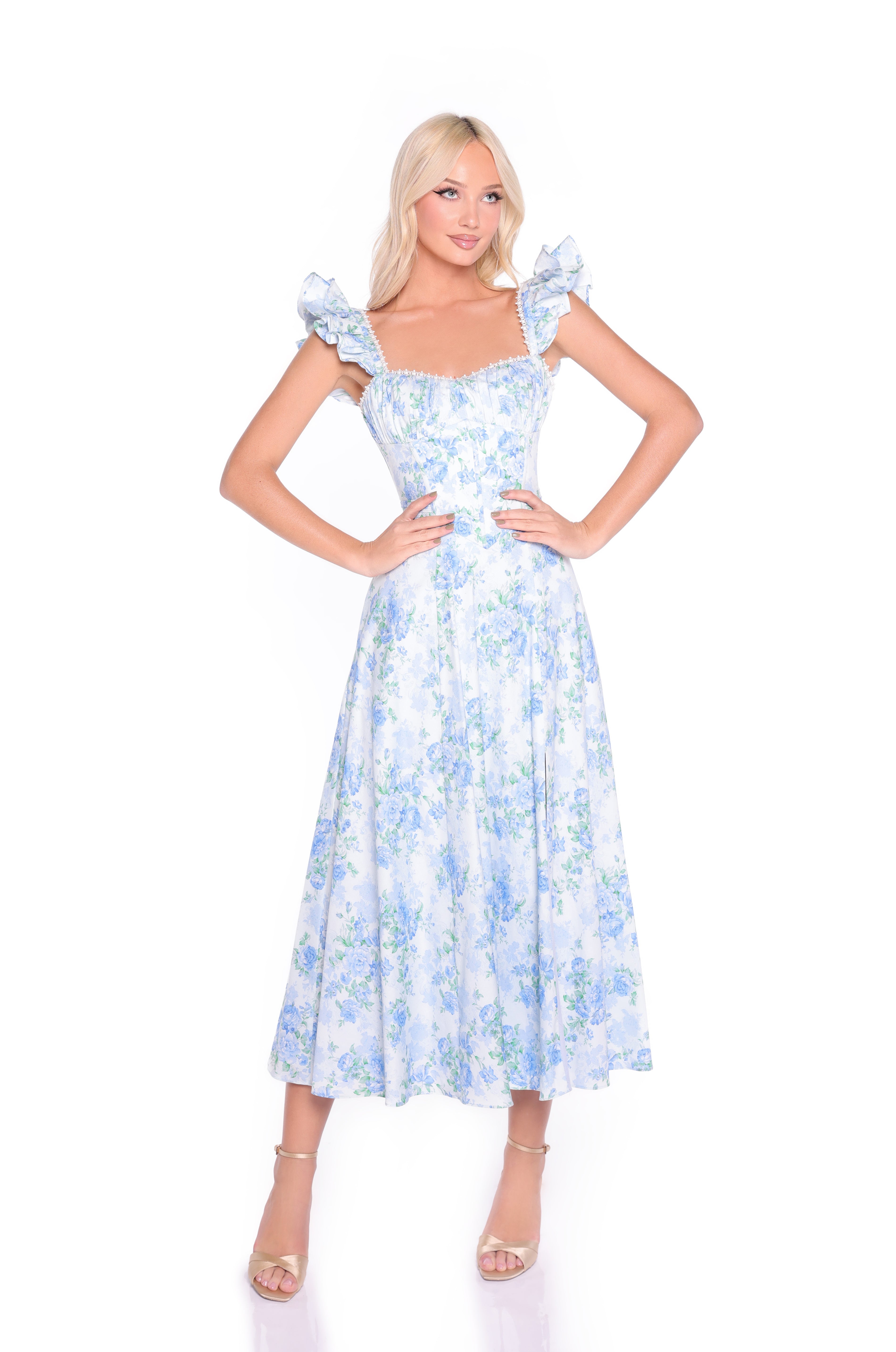 Woman wearing the Blue Floral Midi Cotton Casual Dress: Carmen, featuring ruffled sleeves and a flowing midi skirt, stands with hands on hips against a white background.